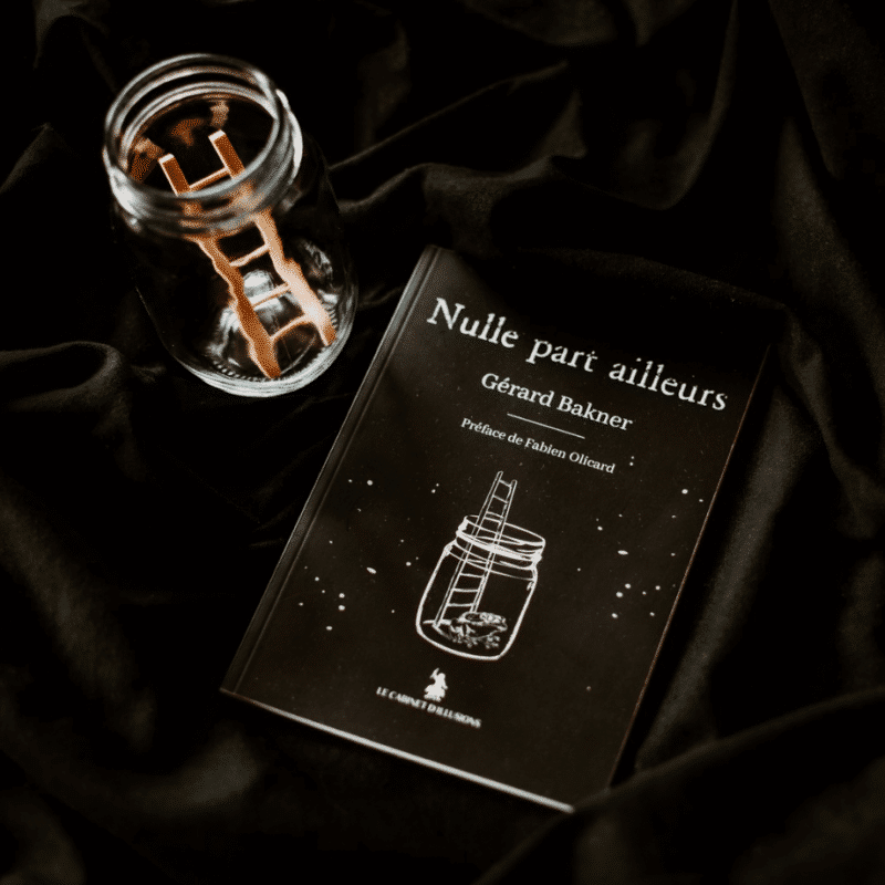 Un livre intitulé "Nulle part ailleurs" de Gérard Bakner est posé sur un tissu sombre à côté d'un bocal avec une petite échelle en bois. La couverture noire présente un bocal rempli d'étoiles.